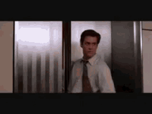 a man in a suit and tie is standing in an elevator and looking out the window .