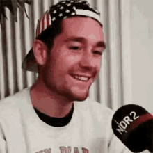 a man wearing a hat and a sweater is talking into a microphone and smiling .