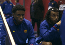 a man wearing a nike jacket sits next to another man wearing a headband