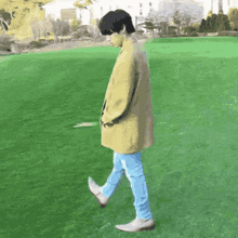 a man in a yellow coat and blue jeans is walking across a grassy field