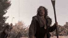 a man in a fur coat is holding a stick in a field