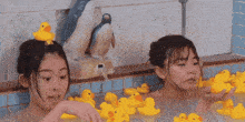 two women are taking a bath with rubber ducks and a penguin statue .