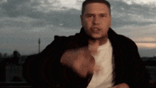 a man wearing a black jacket and a white shirt is pointing at the camera