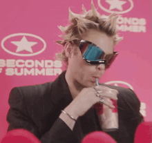 a man wearing sunglasses and a mohawk drinking from a can