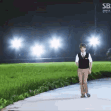 a man is walking down a path in front of a field with a sb sign in the background