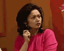 a woman in a pink shirt is sitting at a table with her hands on her chin .