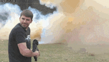 a man is holding a gun in a field with smoke behind him .