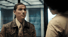 a man wearing a cowboy jacket and tie talks to a woman