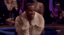 a man wearing a fur coat is sitting in a crowd of people at a party .