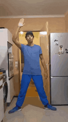 a man in a blue shirt and blue pants is standing in front of a refrigerator .