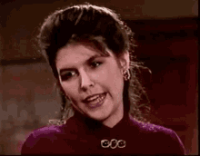 a woman in a purple sweater and earrings is smiling and looking at the camera .
