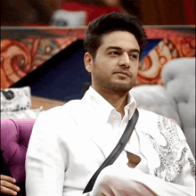 a man in a white suit sits on a purple chair