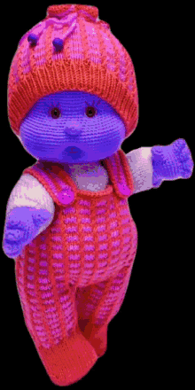 a purple and pink knitted doll with a red hat and overalls