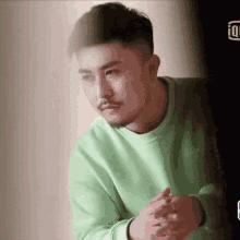 a man with a beard is wearing a green sweater with his hands folded .