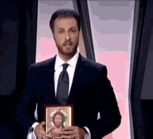 a man in a suit and tie holds a picture of jesus in his hands