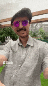 a man wearing a gray shirt and purple sunglasses is smiling .