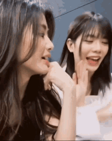 two girls are sitting next to each other and one of them is biting the other 's face .