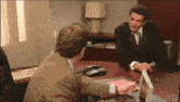 a man in a suit sits at a table with another man