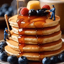 a stack of pancakes with syrup , blueberries , raspberries , and butter .