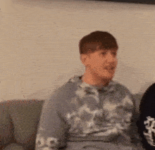 a young man is sitting on a couch wearing a tie dye hoodie .