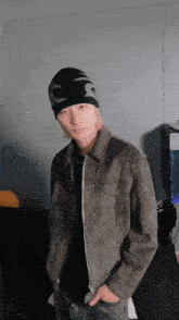 a man wearing a beanie and a jacket is standing in front of a wall