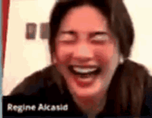 a woman is laughing with her eyes closed and regine alasia is visible in the background .