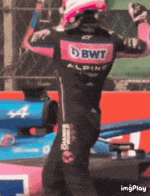 a man in a racing suit with the word bwt on the back is standing in front of a race car .