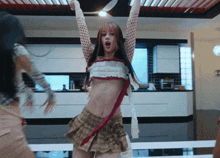 a woman in a plaid skirt is dancing in a kitchen with her arms in the air