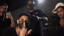 a group of young men wearing face masks are posing for a picture and one of them is giving the middle finger .