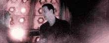 a man in a black suit is standing in a dark room with a purple light behind him .