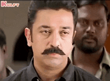 a man with a mustache is standing in front of a group of people .
