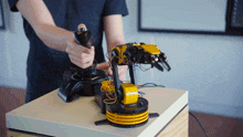 a man is holding a joystick next to a yellow robotic arm