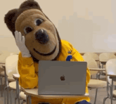 a mascot is sitting at a desk with an apple laptop on it .