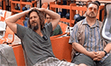 two men are sitting in orange chairs in a bowling alley with their hands on their head .