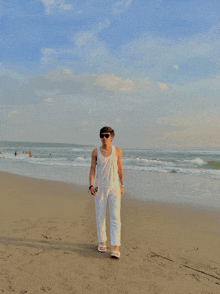 a man wearing sunglasses and a white tank top stands on a beach