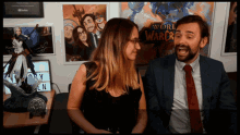 a man and a woman are sitting in front of a world of warcraft sign