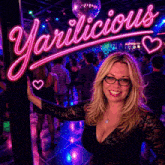 a woman stands in front of a neon sign that says ' yarlilicious '