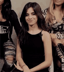 a woman in a black tank top and ripped jeans is sitting next to another woman .