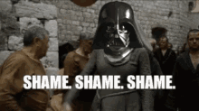 a woman wearing a darth vader helmet is standing in front of a crowd of people and says shame .