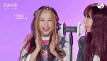 a girl with red hair is smiling next to another girl with blonde hair and a purple background