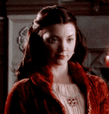 a woman wearing a red jacket and a necklace looks at the camera