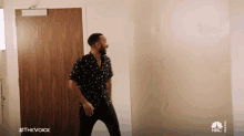 a man in a black shirt is dancing in front of a door that says #thevoice on the bottom