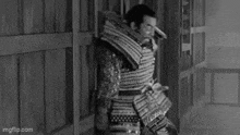 a black and white photo of a samurai holding a bow and arrows .