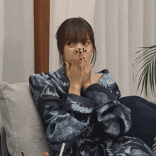 a woman covering her mouth with her hands while wearing a blue robe