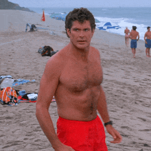 a shirtless man in red shorts is standing on a sandy beach