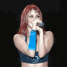 a woman with red hair singing into a microphone wearing a blue wristband