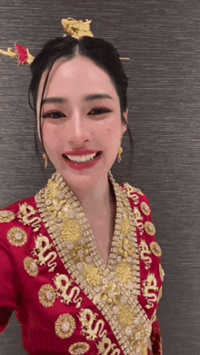 a woman wearing a red and gold embroidered top with chinese writing on it smiles for the camera