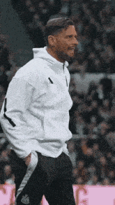 a man wearing a white hoodie and black pants is standing on a soccer field .