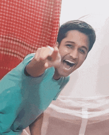 a young man in a blue shirt is pointing at the camera with his mouth open