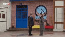 two people standing in front of a building that has trt1 on it